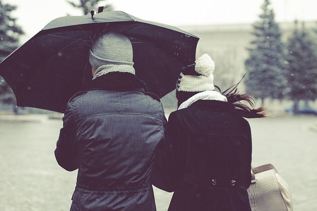 A couple protecting themselves from the wind in a winter storm with an umbrella. 